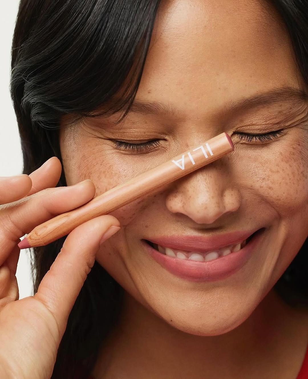 Portrait of adult female smiling with eye liner in front of her closed eye for beauty shot, promoting cosmetics and makeup.
