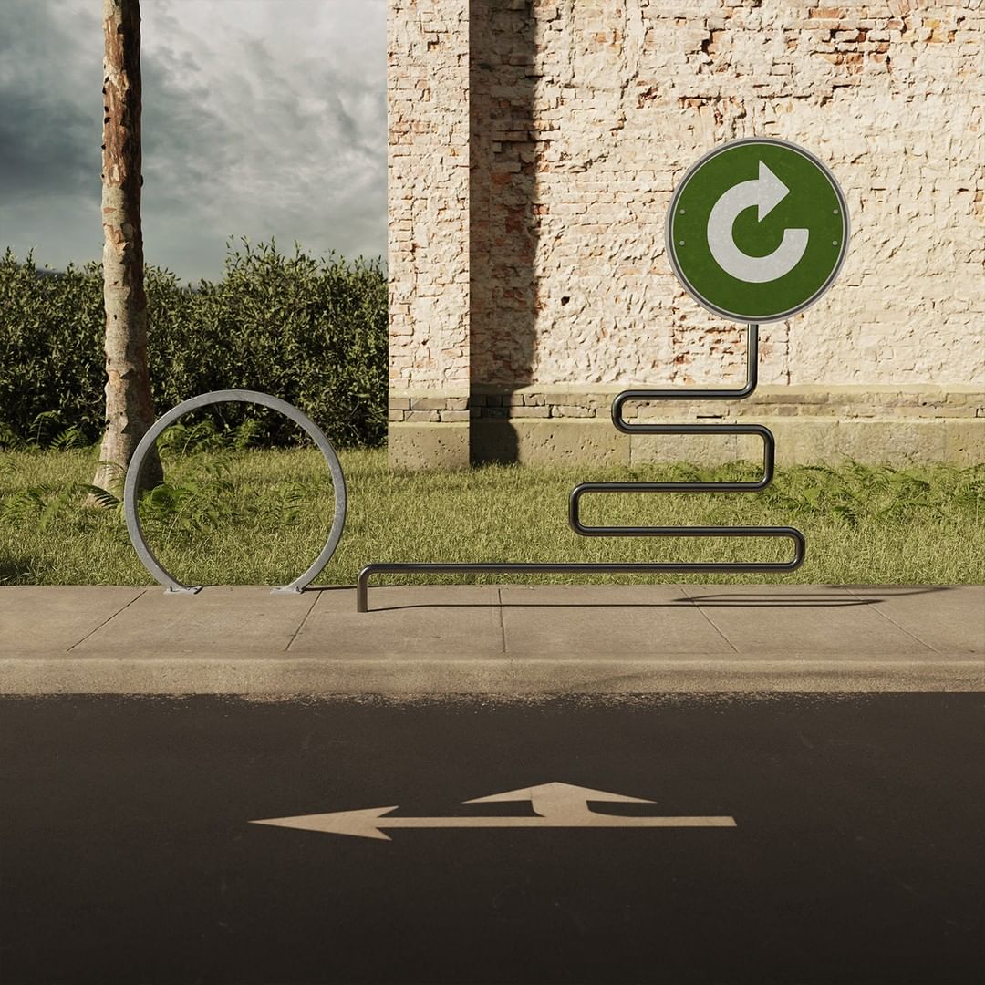 Outdoor image of a bike rack with a green circular sign featuring a white recycle arrow, set against a brick wall and cloudy sky.