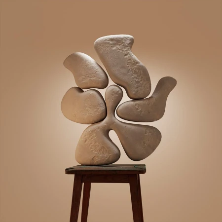 An organic stone sculpture balanced on a wooden stool against a warm neutral studio background.