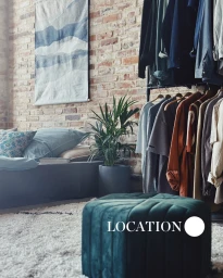 Green velvet pouf in foreground with clothing rack, exposed brick wall, and bed in a modern loft interior