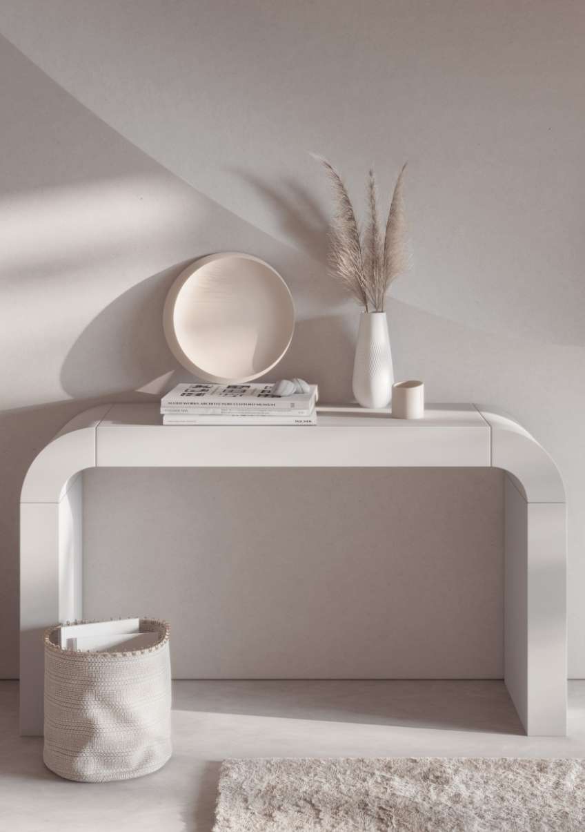 Interior design featuring a white console table with a ceramic vase, plate, books, storage basket, and rug against a white wall.