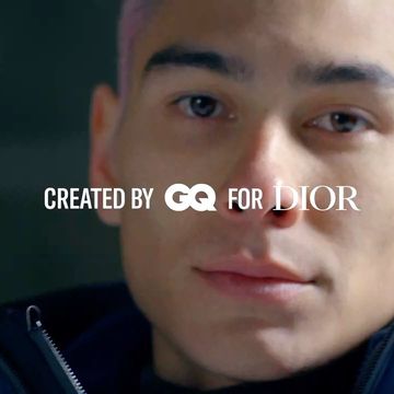 Close-up of a man with short pink hair, wearing a black hooded jacket, set against a dark background, with 'Created by GQ for Dior' text.