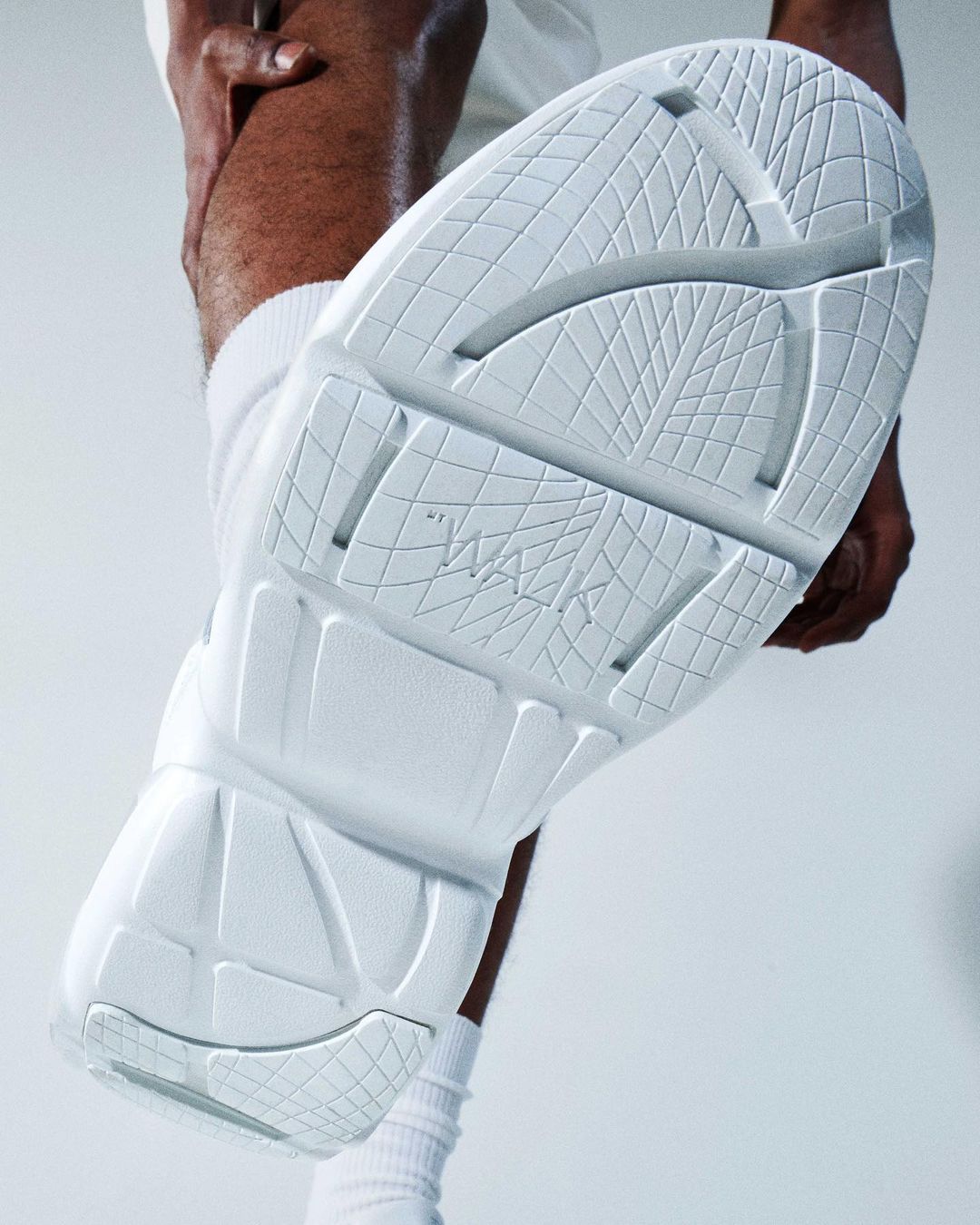 Close-up of a person's foot wearing a white athletic shoe, positioned over the camera, showcasing the shoe's textured sole.