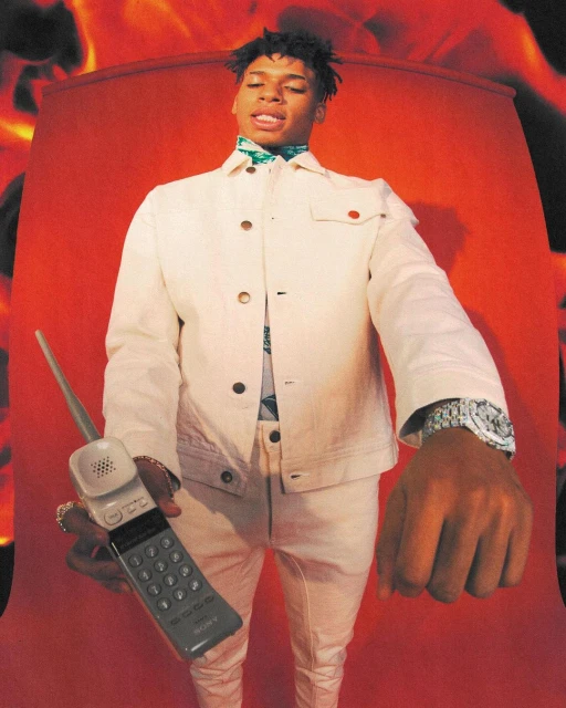 Adult male with a retro mobile phone in a studio with a fiery background, wearing a white denim jacket and pants.