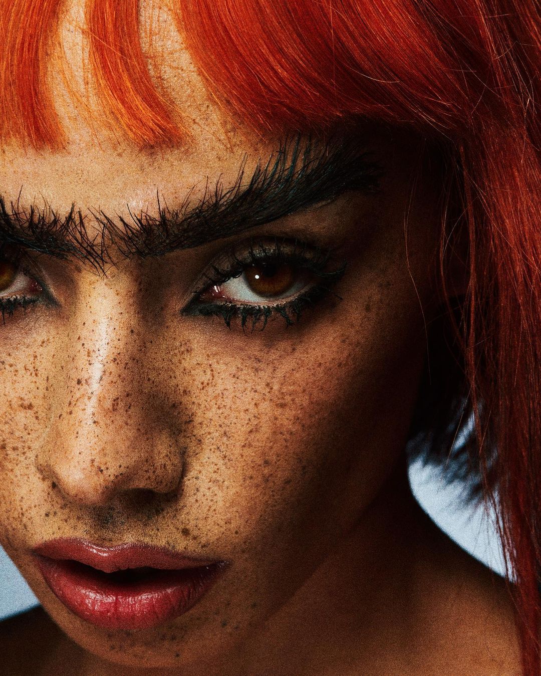 Close-up portrait of a young woman with freckles, brown eyes, and red hair, looking directly at the camera with a neutral expression.