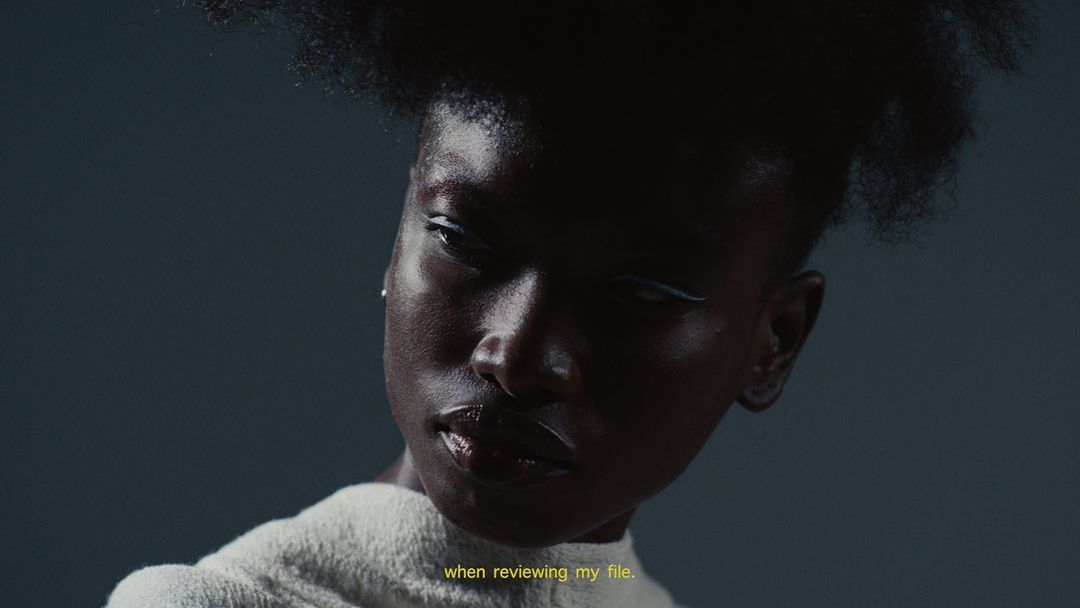 Close-up portrait of an African-American woman with hair in a textured style, wearing white eyeliner and a white collared sweater.