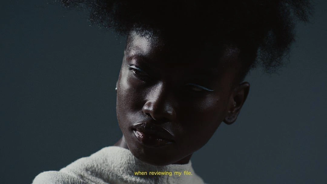 Close-up portrait of an African-American woman with hair in a textured style, wearing white eyeliner and a white collared sweater.