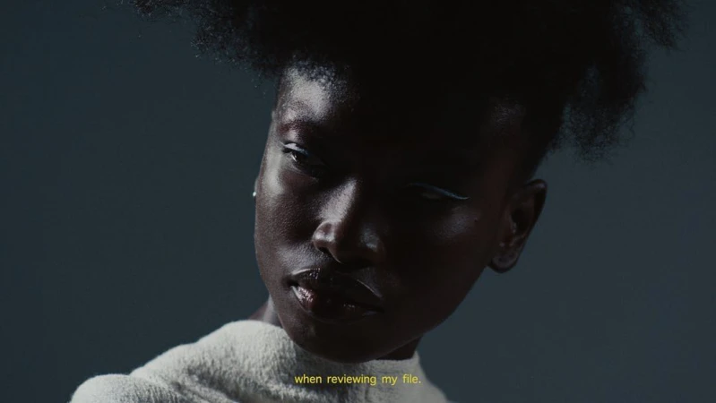 Close-up portrait of an African-American woman with hair in a textured style, wearing white eyeliner and a white collared sweater.