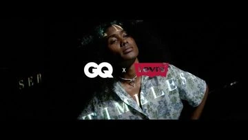 Portrait of an adult female with dark hair, wearing a floral patterned top in front of a dark background with logos.