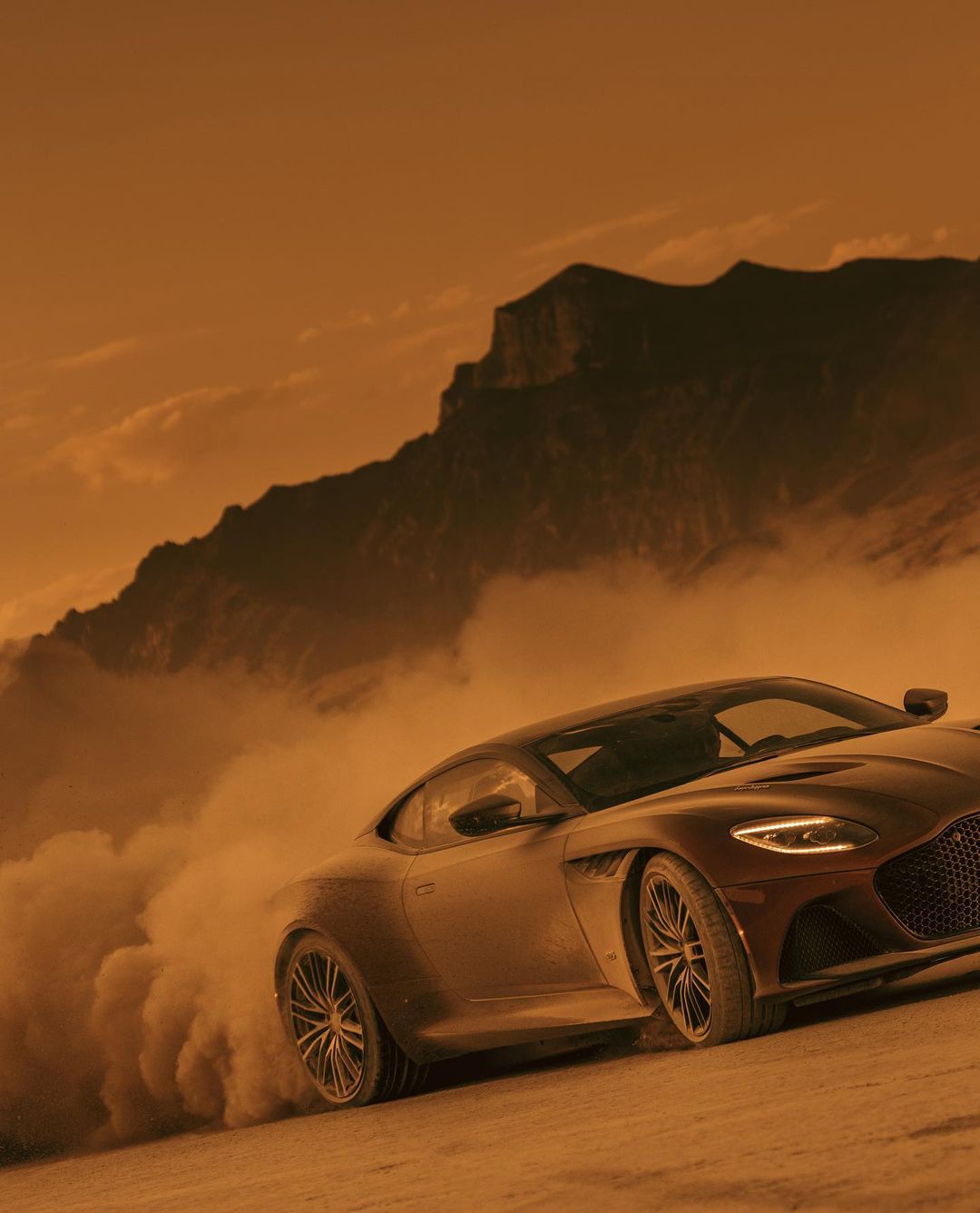 Red sports car drifting in a desert landscape with mountains and dusty sky, showcasing automotive and nature photography.