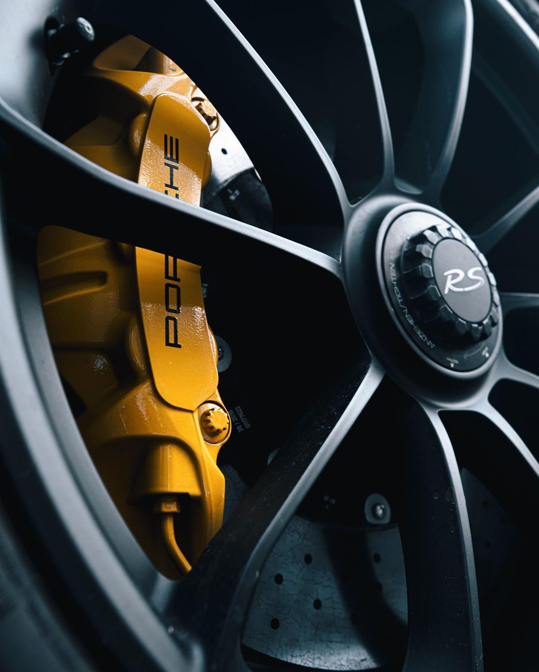 Close-up of a Porsche wheel with yellow brake caliper featuring the brand's name, showcasing automotive engineering and design.