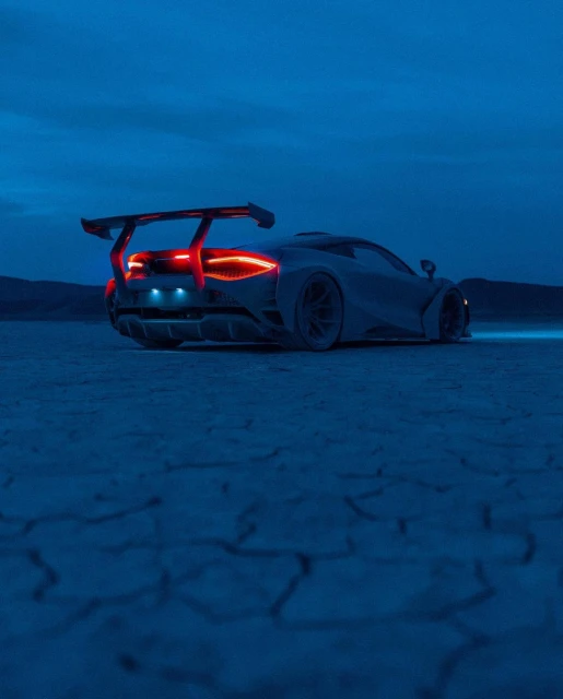 Sleek silver sportscar with a rear spoiler parked on a cracked dry lakebed under a dusk sky, taillights glowing red, artistic render.