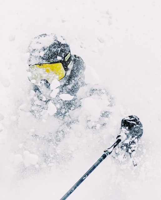 A person in ski gear, wearing a helmet and goggles, is seen from a low angle while skiing in deep, fresh powder snow.
