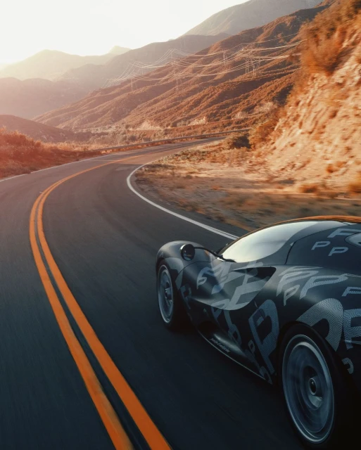 Sportscar races along an open road through a mountain landscape, bathed in warm sunlight. Motion blur on the wheels enhances the sense of speed.