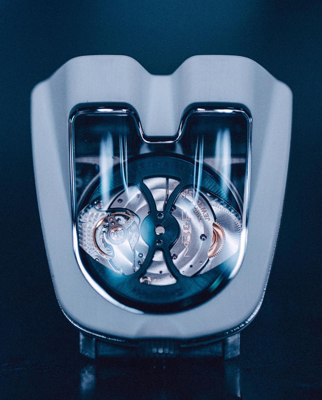 Close-up of a luxury watch with an open-work design, showcasing intricate gears and components, all encased in a sleek, modern white frame.