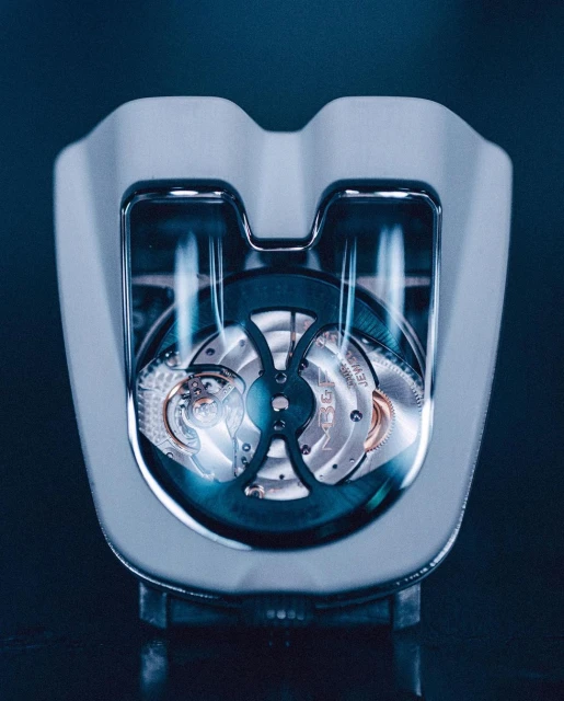 Close-up of a luxury watch with an open-work design, showcasing intricate gears and components, all encased in a sleek, modern white frame.