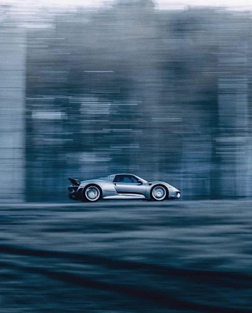 Sleek silver convertible sports car speeding down a rural road surrounded by a blurred forest backdrop on an overcast day.