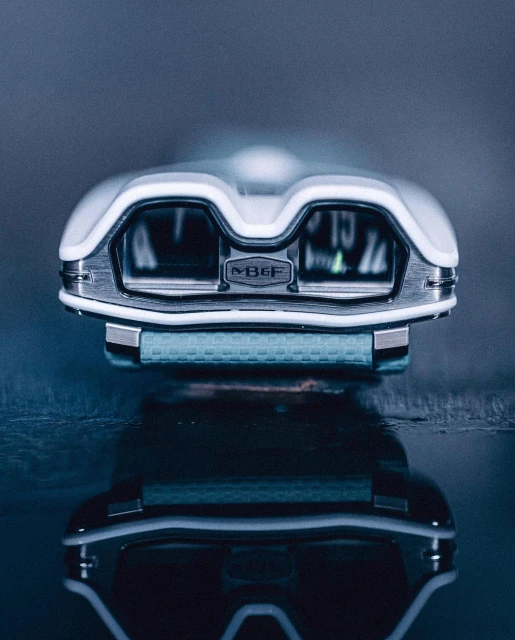 MB&F Horological Machine N°9 'Flow' wristwatch close-up with a white and metal case, displayed on a reflective surface, studio lit.