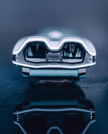 MB&F Horological Machine N°9 'Flow' wristwatch close-up with a white and metal case, displayed on a reflective surface, studio lit.