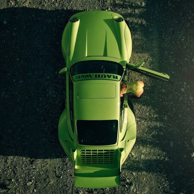 Overhead view of a lime green Rauh-Welt Begriff Porsche parked on a gravel surface with the driver's side door open and a partial view of an adult.