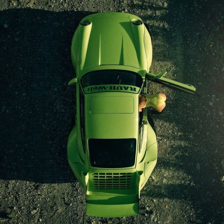 Overhead view of a lime green Rauh-Welt Begriff Porsche parked on a gravel surface with the driver's side door open and a partial view of an adult.