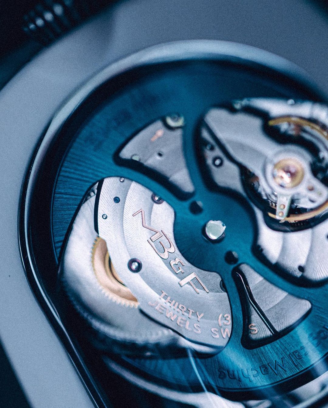 Close-up of the movement and gears inside of a watch, featuring the MB&F logo, blue and silver tones, showcasing intricate details.