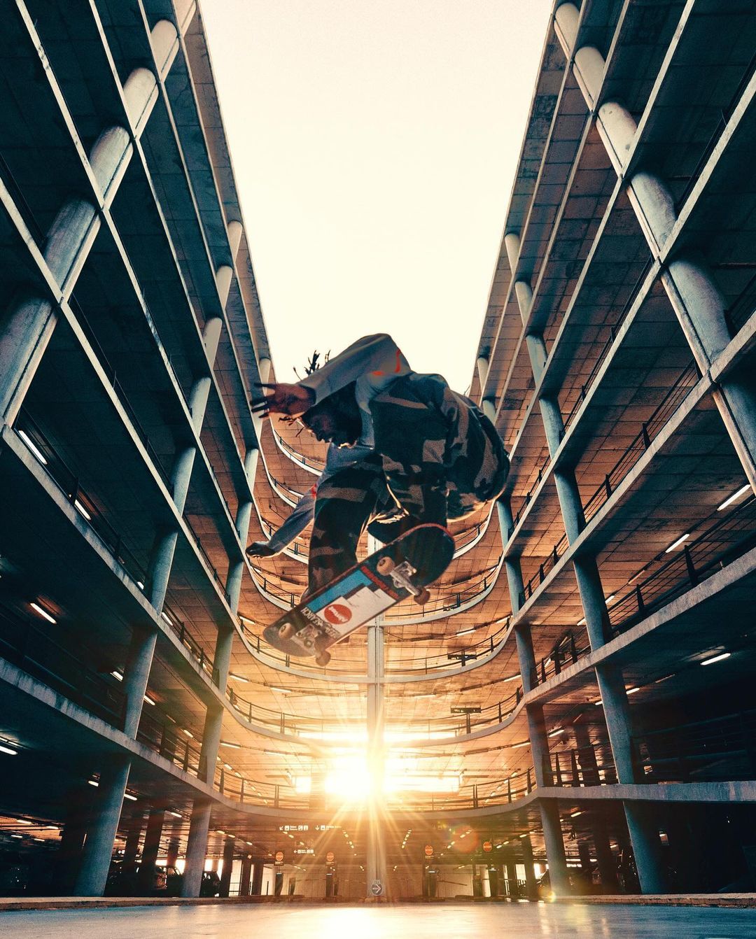 An urban action shot capturing a skateboarder performing a trick mid-air within a parking garage under bright sunlight, creating a dynamic scene.