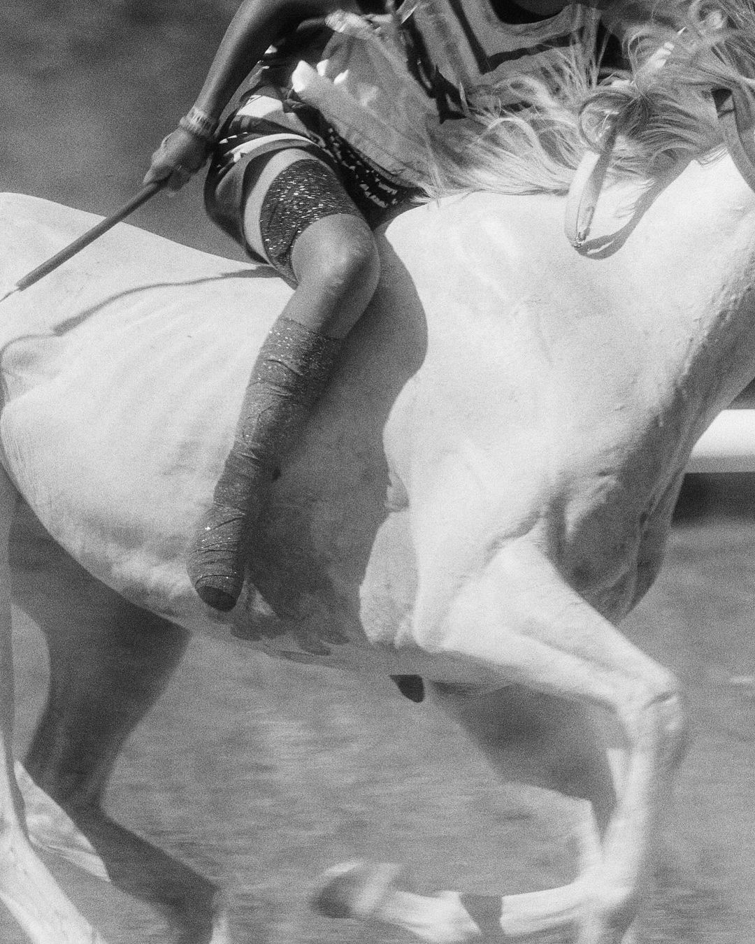 Monochrome image of a person riding a white horse, dressed in traditional attire, captured in motion during a dynamic outdoor scene.