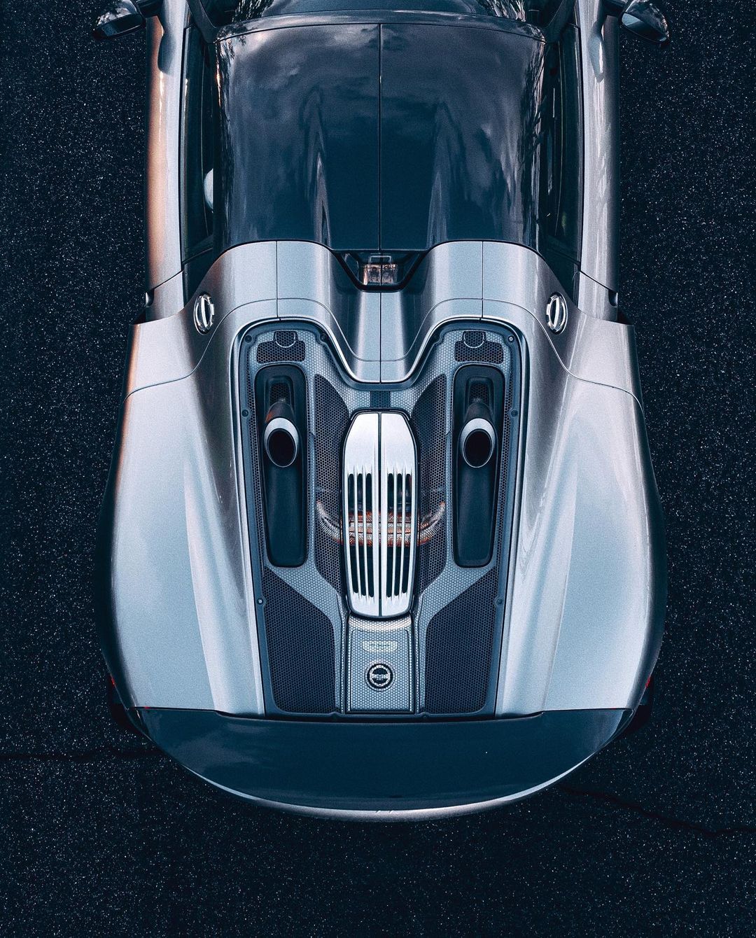 Overhead shot of a gray and silver sports car parked on asphalt, showcasing its sleek design and aerodynamic features in bright lighting.