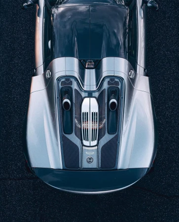 Overhead shot of a gray and silver sports car parked on asphalt, showcasing its sleek design and aerodynamic features in bright lighting.