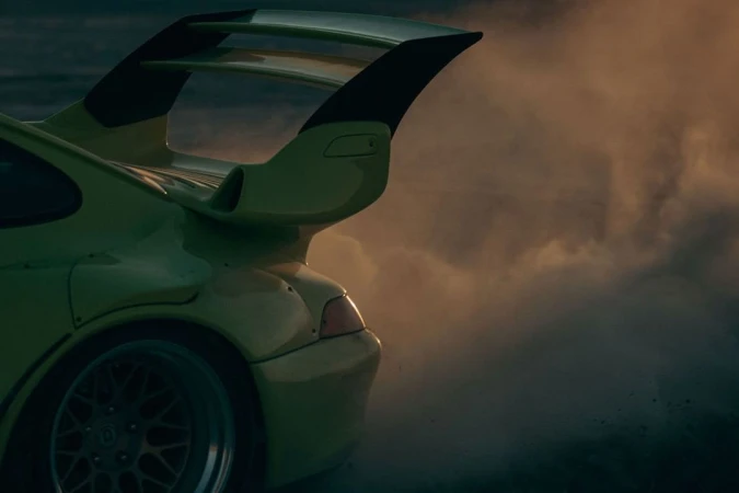 Rear view of a lime green sports car with a spoiler, partially obscured by a cloud of vapor or smoke, suggesting motion and high performance.
