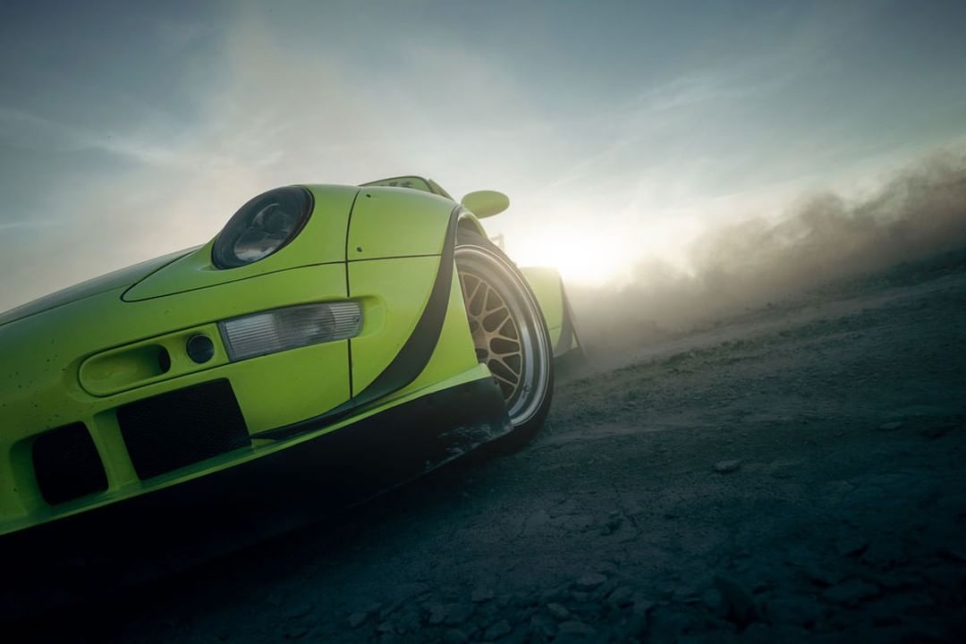 A lime-green sports car is captured at a low angle, surrounded by a cloud of dust, with the sun reflecting on the car.