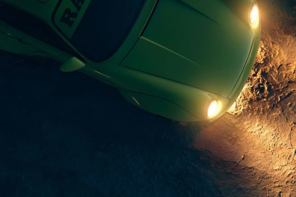 An overhead shot captures a green car with its headlights illuminated on a rugged, dark surface, possibly dirt or cracked pavement.