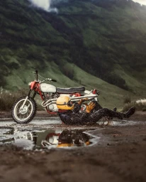 Motorcyclist falling off a dirt bike into a muddy puddle against a lush green mountain slope backdrop.