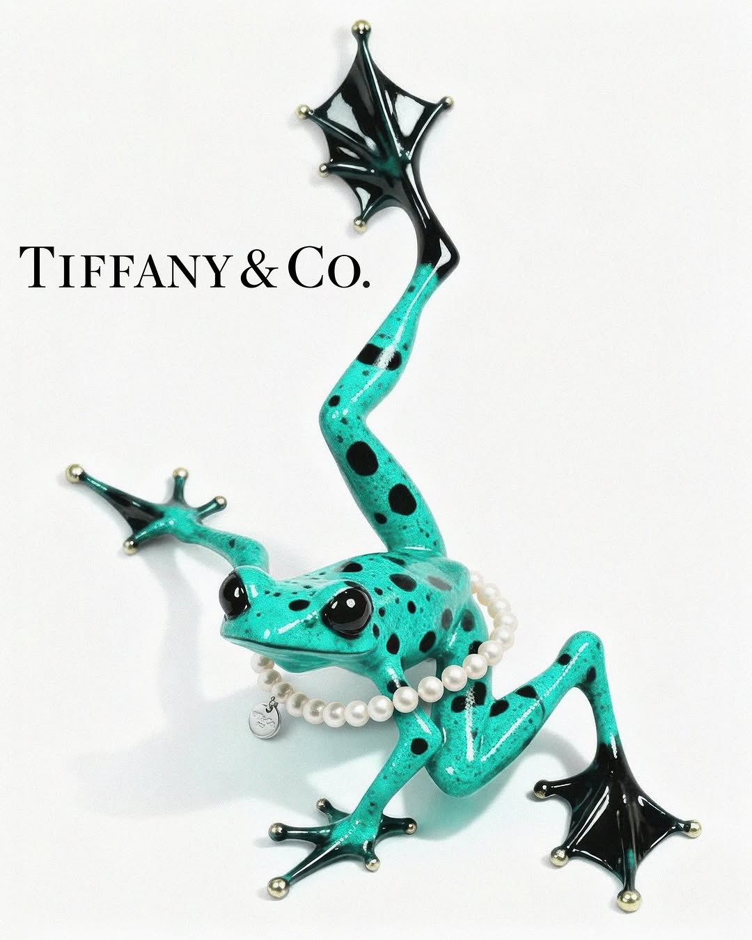 Turquoise poison dart frog with black spots wearing a pearl necklace on a white background, next to the Tiffany & Co. logo.