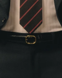 Close up of a man wearing a dark suit jacket, pinstripe shirt, striped tie, black belt, and matching trousers.