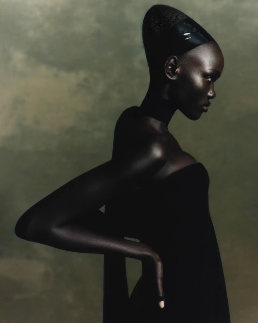 Elegant portrait of a Black woman in a dark dress and headpiece, striking a pose against a muted olive green background in a studio setting.
