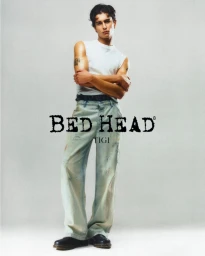 Young man standing with arms crossed wearing a white sleeveless t-shirt and light wash denim jeans against a grey seamless background