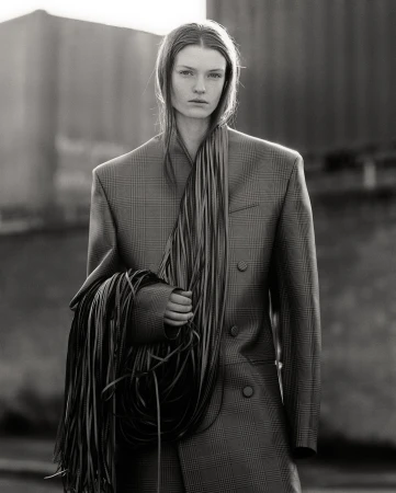 Monochrome portrait of a model in an oversized patterned blazer holding a bundle of fringe cords by Aaron Crossman