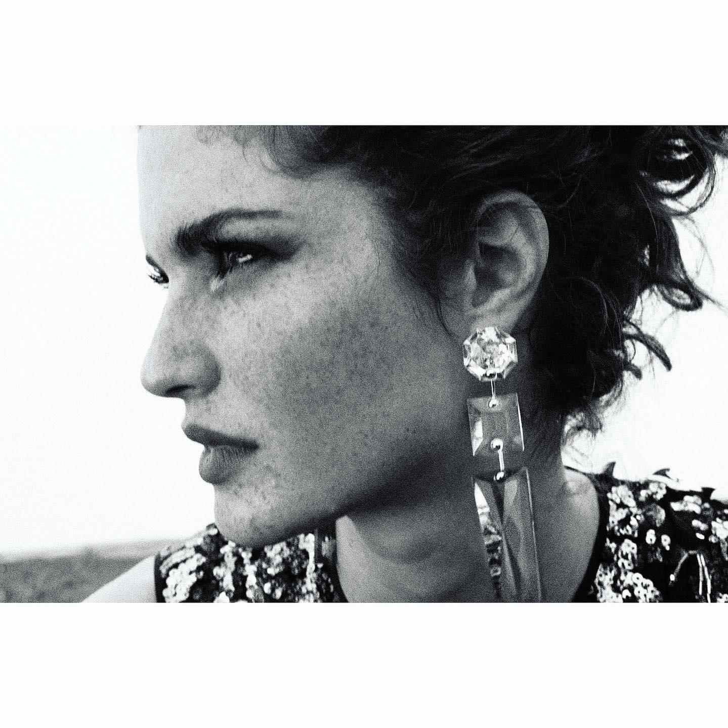 Monochrome close-up shot of a woman in profile wearing large jewel earrings looking to the left against a light background.