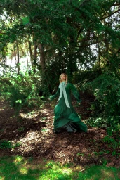 Woman in long green dress with a large bow standing in a dense forest by Sera Zelva