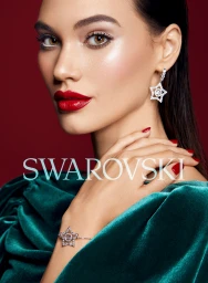 Close-up portrait of a woman wearing star-shaped crystal earrings, a matching star bracelet, and a green velvet top against a dark red backdrop