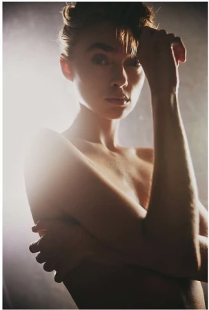 Portrait of a woman with her hand near her hair, lit by warm backlight in a hazy atmosphere captured by Aaron Feaver