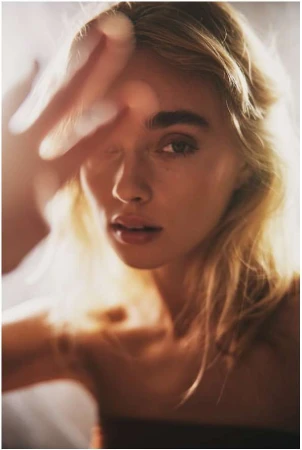Close up portrait of a blonde woman holding her hand near her face with warm backlit sunlight.