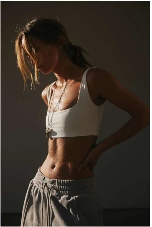 Woman wearing a white crop top and grey sweatpants with water droplets on her skin, photographed by Aaron Feaver.