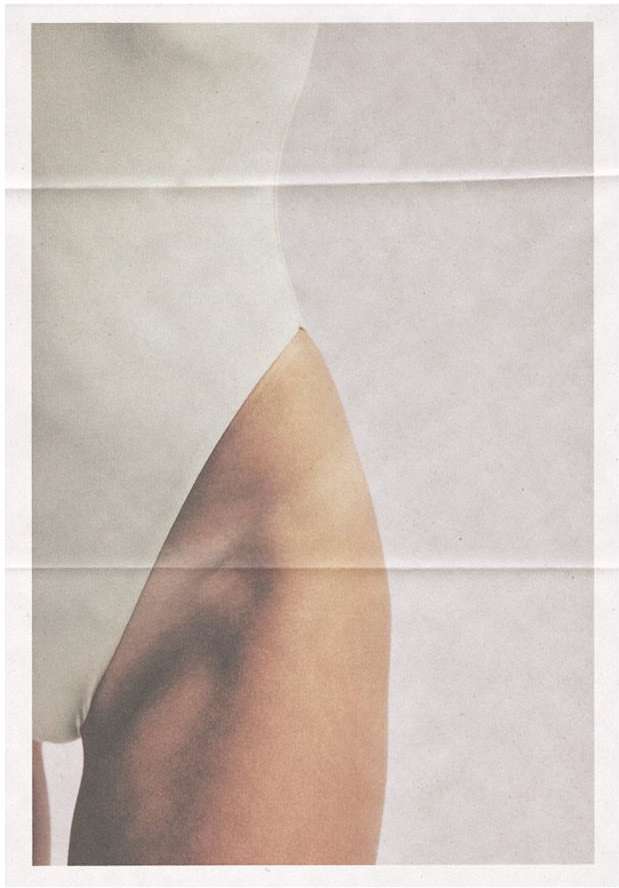Cropped studio shot of a female form in a white leotard, focusing on the thigh and torso, on a folded paper backdrop.