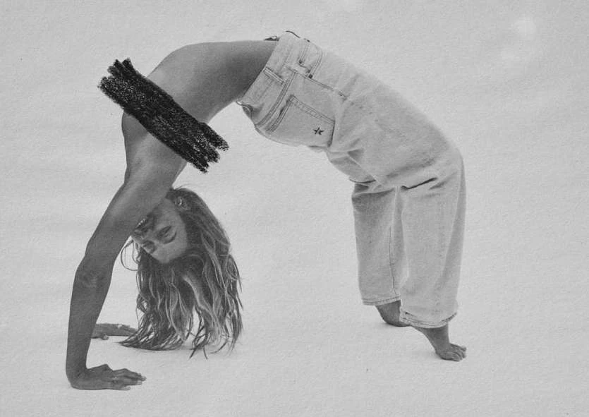Adult woman in a backbend wearing light wash denim pants against a white background, her face and hair are visible.