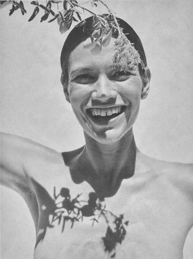 A happy woman smiles at the camera while branches cast shadows across her chest in this black and white portrait.