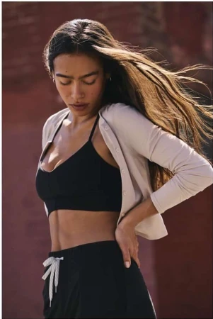 A woman with long flowing hair wearing a cream cardigan and black bralette standing outdoors