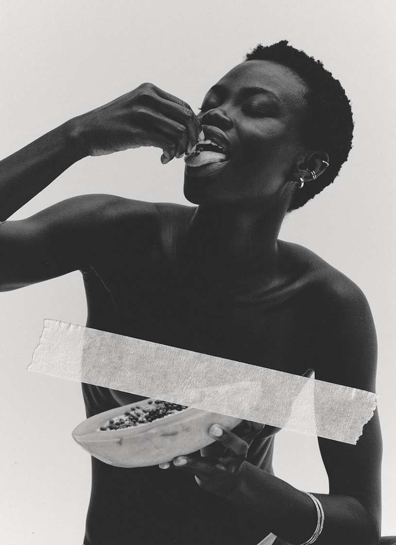 Monochrome portrait of a dark-skinned woman eating papaya, facial expression closed eyes, and a white background and tape.